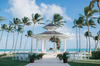 White beach gazebo decorated for wedding ceremony with chairs, palm trees, and ocean view backdrop White beach gazebo decorated for wedding ceremony with chairs, palm trees, and ocean view backdrop