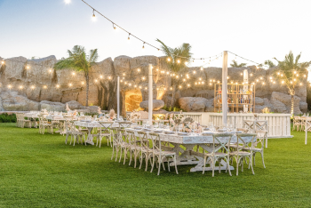 Outdoor wedding reception with long tables, string lights, and bar setup on a landscaped lawn at sunset Outdoor wedding reception with long tables, string lights, and bar setup on a landscaped lawn at sunset