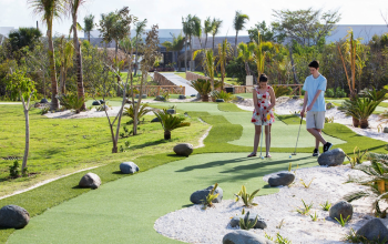 Mini golf course on the resort grounds with guests playing surrounded by tropical landscaping Mini golf course on the resort grounds with guests playing surrounded by tropical landscaping