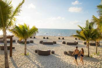 Couple walking along beach with lounge seating and ocean views at Moon Palace The Grand – Cancun.