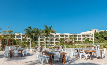 Outdoor reception setup with long tables, wooden chairs, and tropical décor on a terrace.