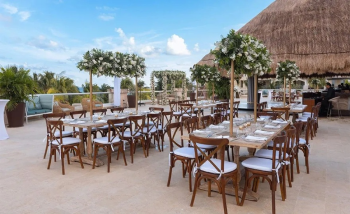 Outdoor terrace wedding reception with round tables and resort buildings in the background.
