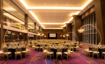 Elegant ballroom wedding reception with round tables, gold chairs, and ambient lighting.