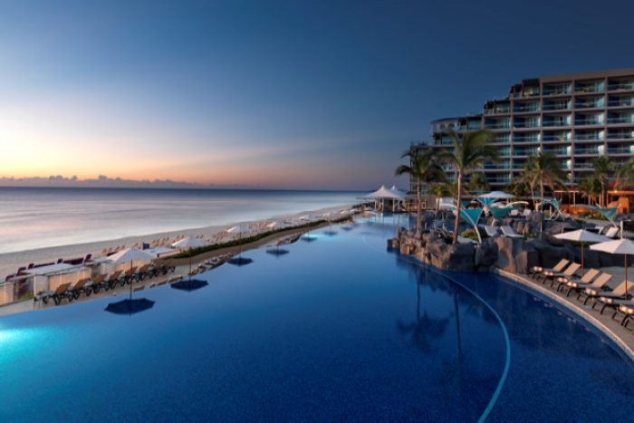 Beachfront walkway with lounge chairs and ocean views alongside resort pool in Cancun