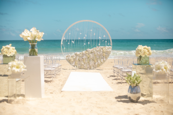Modern beach wedding ceremony with circular arch, white florals, and acrylic chairs for Modern Enchantment package