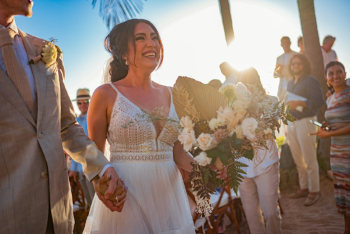 Bride smiling during a beachfront destination wedding ceremony while holding a bouquet and walking with her partner. Bride smiling during a beachfront destination wedding ceremony while holding a bouquet and walking with her partner.