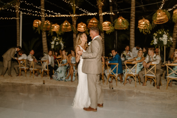 Newlywed couple sharing their first dance
during an outdoor wedding reception beneath string lights and tropical décor. Newlywed couple sharing their first dance
during an outdoor wedding reception beneath string lights and tropical décor.